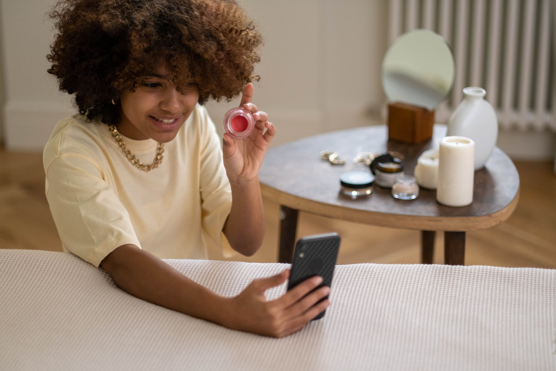 woman in yellow shirt showing a beauty product while recording on smartphone