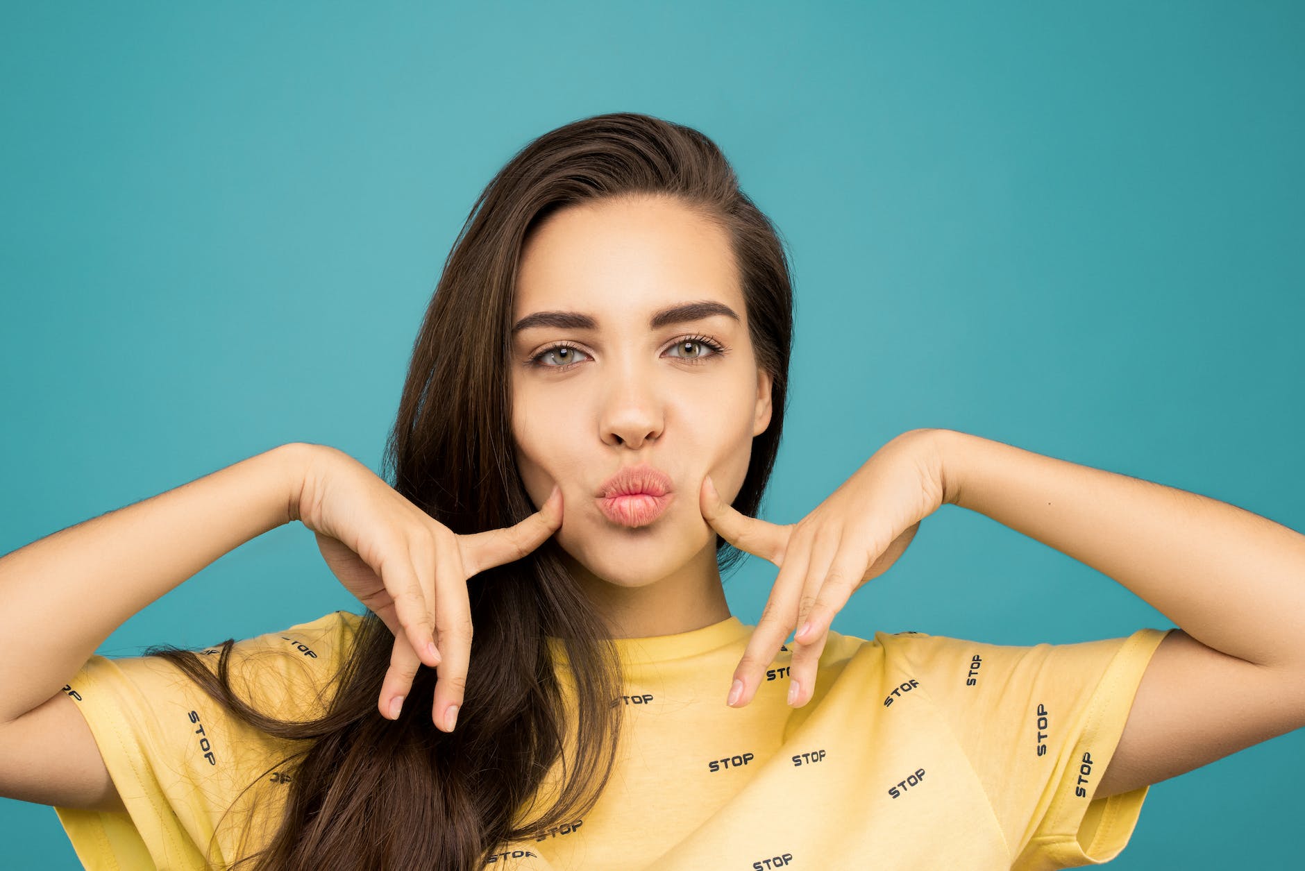 portrait photo of woman in yellow t shirt posing with her fingers on her cheeks