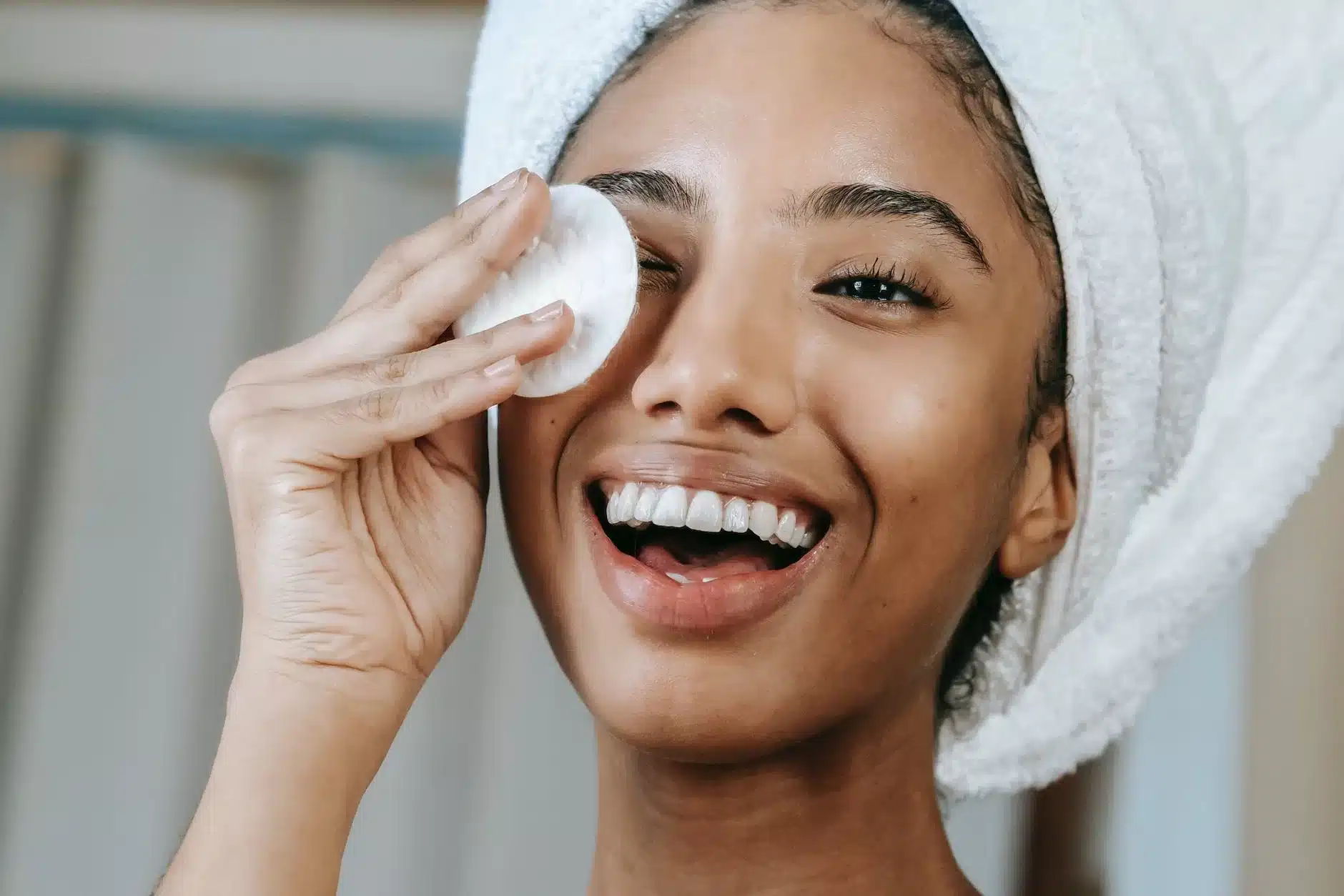 ethnic smiling woman wiping face with cotton pad