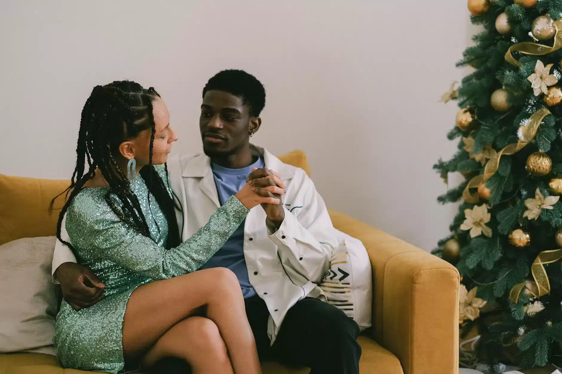 a couple sitting on the sofa next to the christmas tree