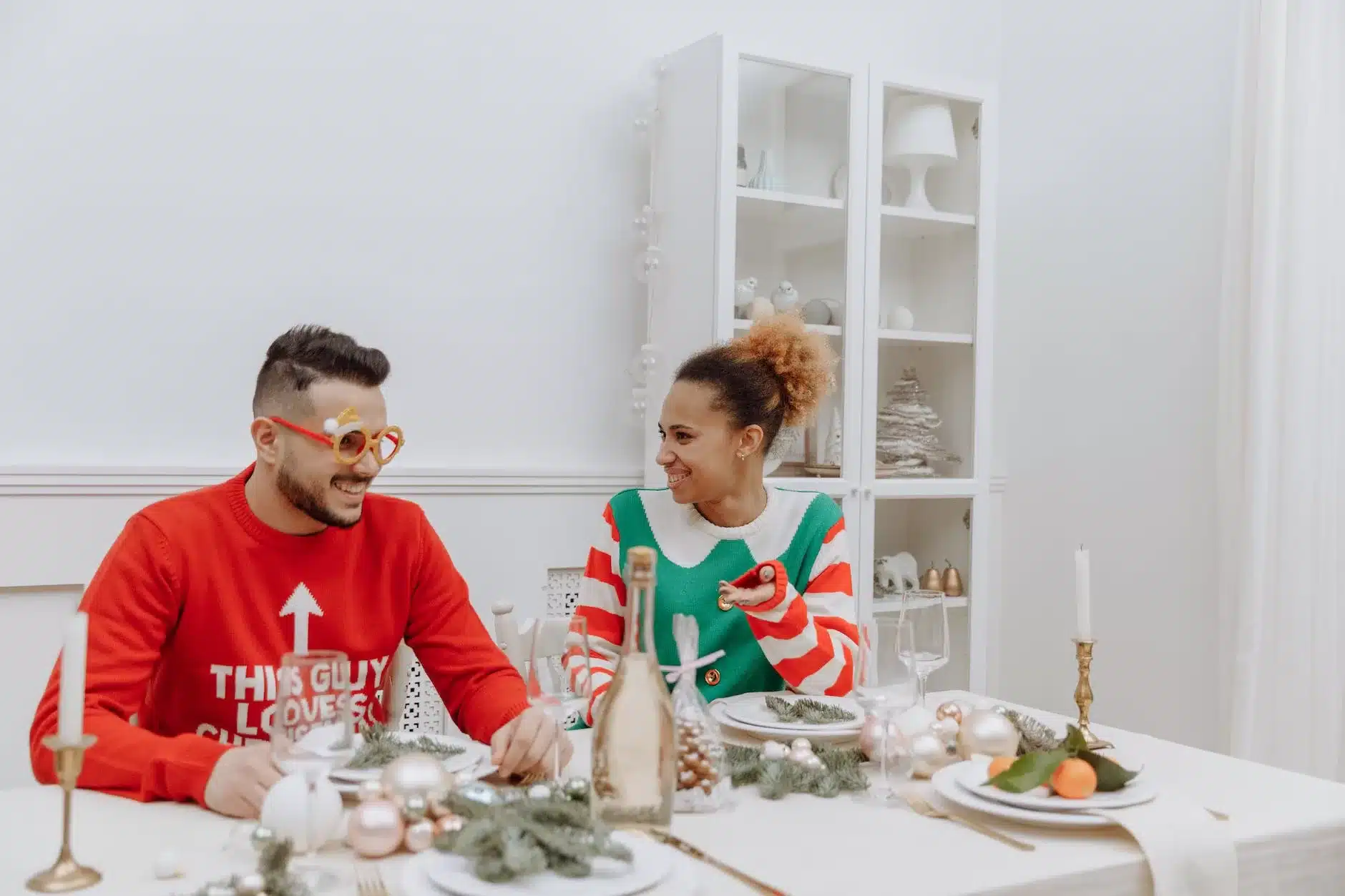 a couple in ugly christmas sweaters sitting at the table